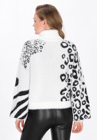 Pulover alb pufoș cu modele de leopard și zebră negre, guler înalt și mâneci largi. Material texturat cu un aspect moale și confortabil.