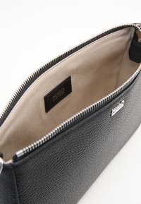 Sort tekstureret læder clutch taske med sølvfarvet lynlås, beige indvendig foret og et lille sort label med brandnavnet "Hugo."
