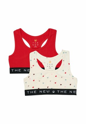 Deux brassières de sport pour filles, une rouge unie et une blanche avec des cœurs multicolores, toutes deux avec des bandes élastiques noires portant la mention "THE NEV."