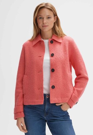 Coral wool-blend jacket with a collared neck, front button closure, two side pockets, and textured fabric. Styled with a white shirt.