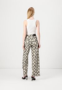Pantalones de pierna ancha con estampado de serpiente, que presentan un patrón en beige y negro, cintura alta y detalle de cinturón. Combinados con una blusa sin mangas blanca.