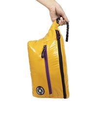Bolsa aislante amarilla con cremallera y acentos morados, que cuenta con un asa negra y un parche de logo en el lateral. Forma rectangular.