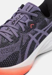 Chaussure de sport violette avec une tige en mesh texturé et des accents noirs. Présente des lacets violets, une semelle blanche et un détail de talon orange.