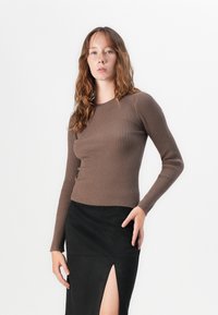 Top lungo a maniche lunghe marrone con righe, design aderente. Abbinato a una gonna nera con uno spacco laterale. Texture liscia e colori contrastanti.