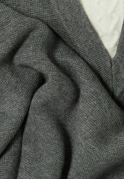 Pull en tricot gris avec une finition texturée et douce. Présente un col en V et est légèrement drapé, avec des détails visibles dans le tissu.