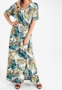 Robe maxi à manches courtes, présentant un motif de feuilles tropicales en teal et or sur un fond blanc ; cintrée à la taille avec un lien.