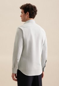 Lichtgrijze langemouwen shirt met een op maat gemaakte kraag, subtiele textuur, gebogen zoom en geknoopte mouwen met kleine geborduurde accenten.