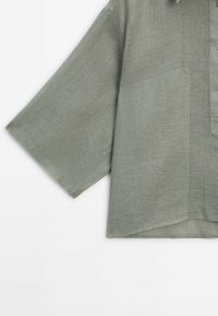 Green linen short-sleeve shirt with a collar, featuring a front pocket and textured fabric. Casual, loose fit with a straight hem.
