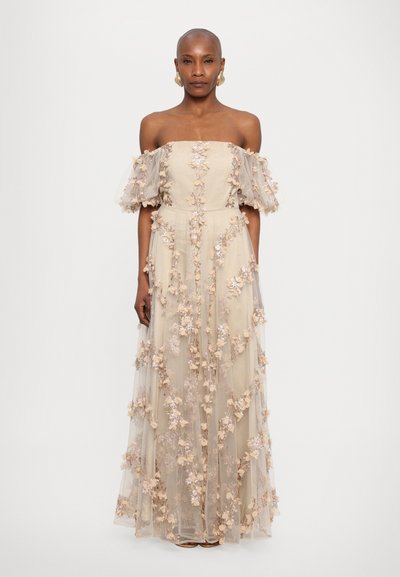 Beige off-shoulder-mekko, jossa on tulle-puffhihat, koristeltu pehmeillä vaaleanpunaisilla ja laventelilla kukka-aplikoilla, virtaava lattiaan ulottuva malli.