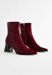 Crvene i crne antilop čizmice s leopard printom, s oštrim vrhom i robusnom crnom potpeticom. Zatvaranje s patentnim zatvaračem sa strane.