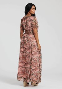 Abito maxi in tessuto semi-trasparente con un motivo di foglie rosa e verdi, maniche corte e vita elastica. Indossato con sandali con zeppa color beige.