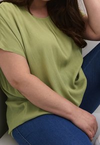 Lys grøn, tekstureret top med korte ærmer, afslappet pasform, parret med blå denim bukser, som blødt hænger ned i siderne.