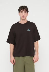 Μαύρο βαμβακερό μπλουζάκι με άνετη εφαρμογή, με μικρό τουρκουάζ λογότυπο στο στήθος. Το ύφασμα είναι λείο με κοντά μανίκια.