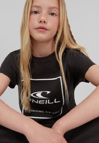 Zwarte katoenen t-shirt met korte mouwen en een ronde halslijn, voorzien van een wit logo en tekstontwerp op de voorkant.