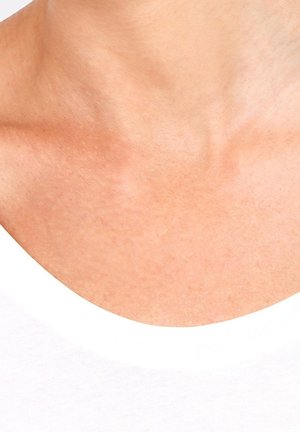 Gros plan sur le cou et le haut de la poitrine d'une personne, montrant une peau lisse au-dessus de l'encolure d'une chemise blanche.