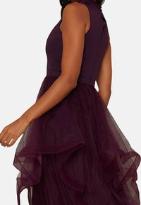 Burgundy-mekko, jossa on kapea vartalo ja kerroksellinen tüllihame, jossa on röyhelöreunat tekstuuria ja liikettä varten.