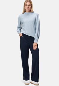 Maglione azzurro chiaro a trama con colletto alto e maniche voluminose, abbinato a pantaloni a gamba larga blu navy e sneakers bianche.