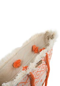 Bolsa de mimbre con intrincados patrones naranjas, base color crema, borde con flecos y asas de cuerda. Presenta pompones decorativos y un cierre de cremallera.