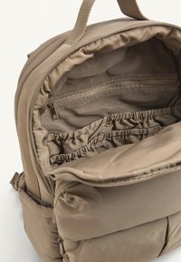 Vnútro svetlohnedého textilného batohu, ktoré obsahuje sieťové vrecká, elastickú organizáciu a zipsom uzatvárateľný priečinok na uloženie.