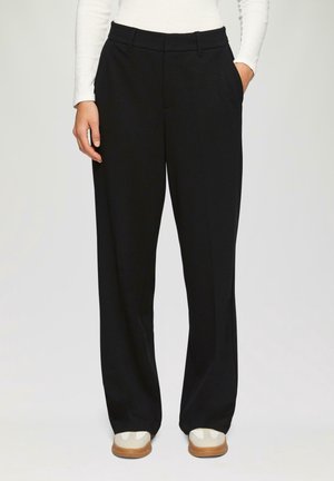 Sorte, vide bukser med sidelommer, glat tekstur og skræddersyet talje; parret med lyse sko.