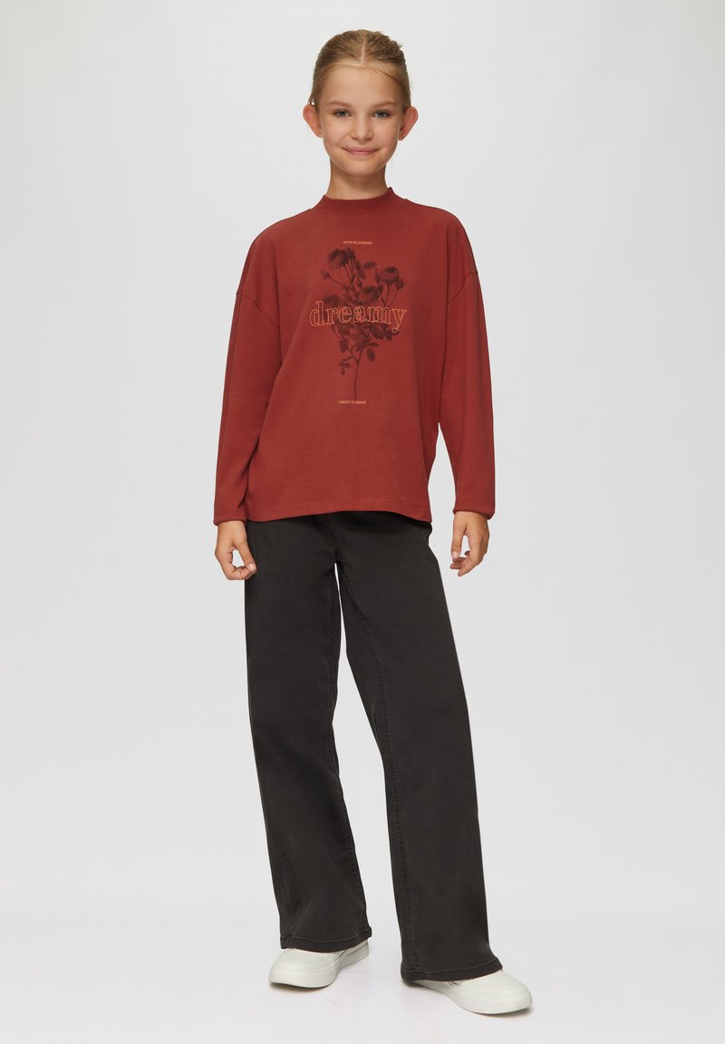 Rotes Langarmoberteil mit dem Aufdruck "dreamy" und floralem Design, kombiniert mit schwarzen weit geschnittenen Hosen und weißen Turnschuhen. Glatte Stofftextur.