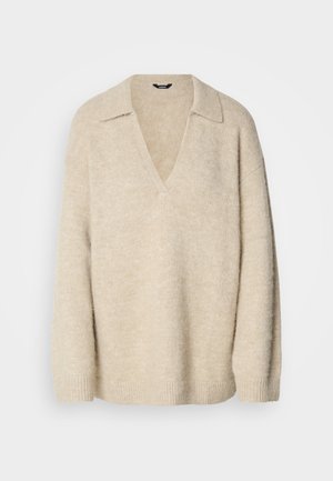 Pull en tricot beige avec un col en V et un col, présentant des manches relâchées et des poignets côtelés. Texture douce avec une finition légèrement duveteuse.