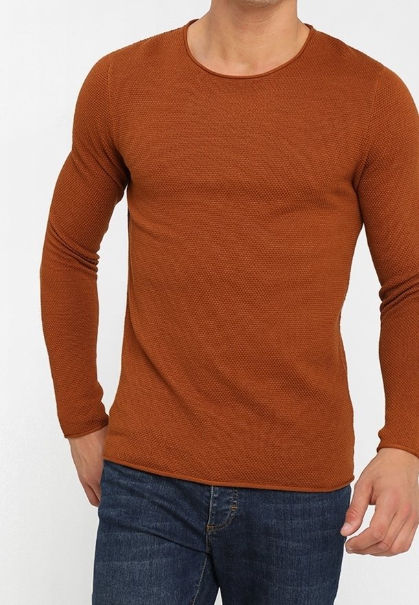 Chemise marron texturée à manches longues avec un col rond, associée à un jean en denim bleu. Le tissu semble tricoté et ajusté.