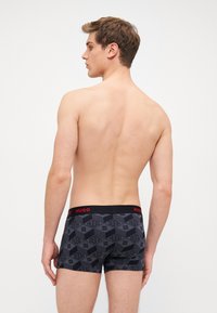 Boxers para hombre en negro con un patrón geométrico. La cinturilla presenta un logo rojo de "HUGO". Tela suave y elástica con un ajuste ceñido.