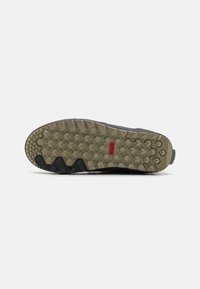 Suela de zapato deportivo negra con patrón texturizado, que presenta un diseño de agarre en forma de hexágono. Logotipo de la marca en rojo cerca del centro. Material de goma duradera.