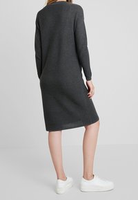 Vestito grigio scuro a maniche lunghe con una texture a coste, che termina appena sopra il ginocchio. Il modello indossa sneaker bianche per contrasto.