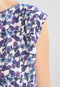 Blusa de patrón floral con fondo blanco, presenta flores azules, moradas y rosas. Mangas cortas y tela suave y ligera.