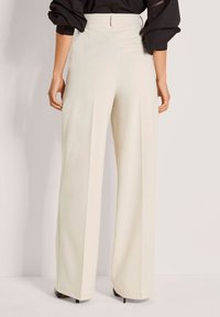 Wijde broekspijpen in crème stof met een gladde textuur en hoge taille. Voorzien van een verborgen ritssluiting aan de achterkant en nauwkeurig genaaide naden.