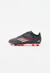 Schwarzer Fußballschuh mit pinken Akzenten, strukturiertem Obermaterial und einem sicheren Klettverschluss. Mit drei diagonalen weißen Streifen an der Seite.
