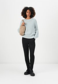 Lichtblauwe textuurtrui, zwarte tapered broek en zwarte veterschoenen. Het model draagt een beige schoudertas.