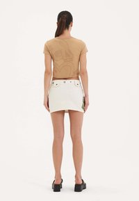 Beige crop top med skullprint, parret med en hvid mini skirt med rå kant og grønne blomsterdetaljer, iført sorte platform-sandaler.
