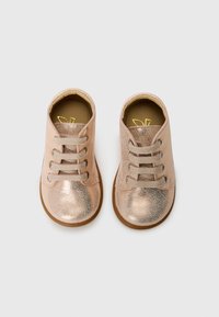 Zapatos infantiles con cordones en un metálico oro rosa con un acabado texturizado; punteras redondeadas y suela de goma marrón. Acentuados con cordones beige.