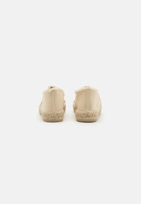 Beige Leinensandalen mit ausgefransten Kanten, gewebten Jutesohlen und einem flachen Design. Die Rückansicht zeigt keine Beschläge oder Akzente.