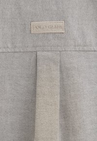 Grått tyg med en texturerad väv, med en beige rektangulär etikett som säger "POLO CLUB" sydd på ytan.