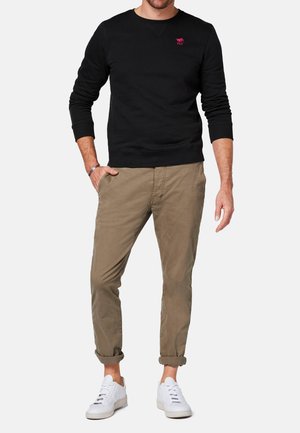 Pullover in cotone nero con colletto rotondo e un piccolo logo rosa, abbinato a pantaloni beige chiaro e sneakers bianche. Design semplice e aderente.