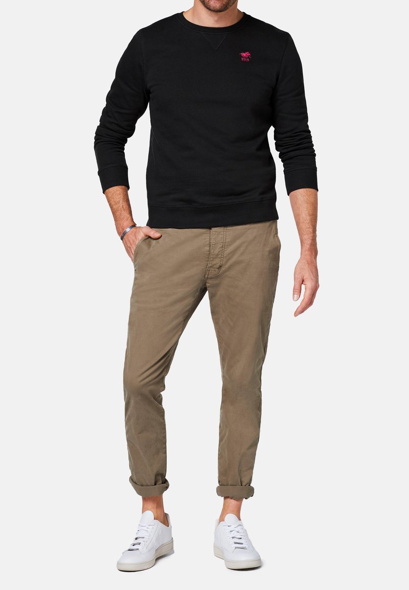 Czarny bawełniany sweatshirt z okrągłym dekoltem i małym różowym logo, w połączeniu z jasnobrązowymi chinosami i białymi sneakersami. Prosty, dopasowany fason.