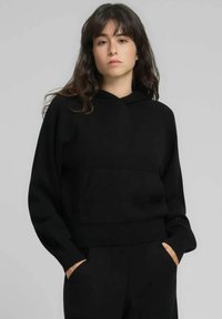 Sweat à capuche noir court en tissu doux, avec une poche frontale, des poignets larges et une capuche à cordon. Design simple et décontracté.