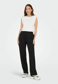Witte cropped tanktop gecombineerd met zwarte elastische broeken. Het model draagt witte en zwarte sneakers. Eenvoudige, gladde stof, comfortabele pasvorm.