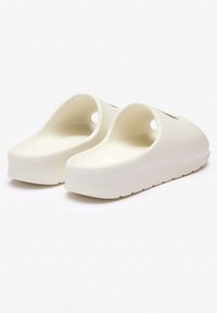 Zuecos blancos de goma con amplias aberturas y un diseño suave y redondeado. La suela es ligeramente elevada y cuenta con un fondo texturizado para proporcionar agarre.