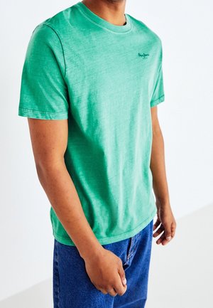 Camiseta verde de manga corta hecha de algodón, con cuello redondo y un logo sutil impreso en el pecho, combinada con vaqueros azul denim.