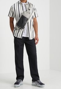 Pasiasta koszula z krótkim rękawem w kolorze białym i granatowym, czarna torba na ramię o teksturowanym wykończeniu, czarne spodnie oraz szare trampki z poduszką powietrzną.