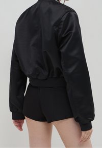 Czarna satynowa kurtka bomberka o luźnym kroju, z elastycznymi mankietami i pasem; gładka faktura i minimalistyczny design.