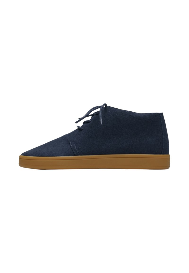 Botas chukka de ante azul marino con punta afilada, diseño de cordones y suela de goma en color marrón claro, con una textura suave y detalles de costura mínimos.