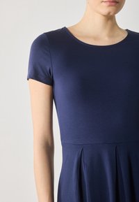 Navy blue short-sleeve dress made of soft fabric, featuring a round neckline and pleated design at the waist. Smooth texture and fitted top.