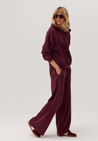 Burgundowa bluza z luźnym krojem, z detalem w postaci sznurka, oraz szerokie spodnie w dopasowanym kolorze. Teksturowany materiał o gładkim wykończeniu.