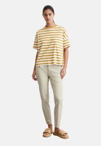 Gestreepte gele en witte oversized T-shirt, beige slim-fit broek en tan gestructureerde sandalen. Rechte silhouet, casual ontwerp, zachte stof.